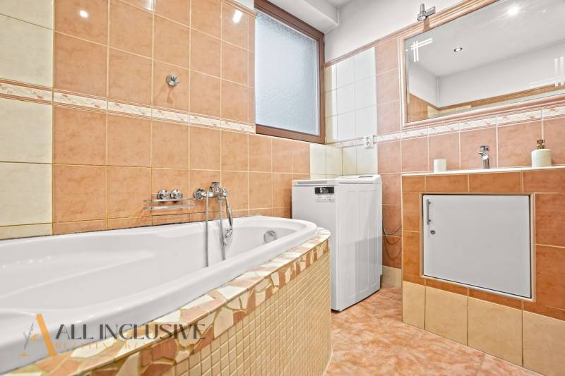 A bathroom in a family house with a bathtub, a washing machine, and tiles in warm colors.