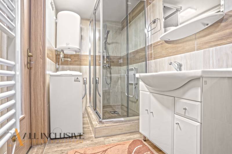 A bathroom in a family house with a washing machine, a shower cabin, and a floor with a wooden decor.