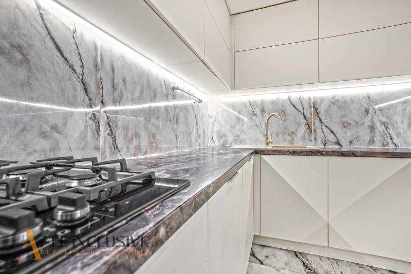 A family house kitchen with a marble wall, gas stove, and sink.