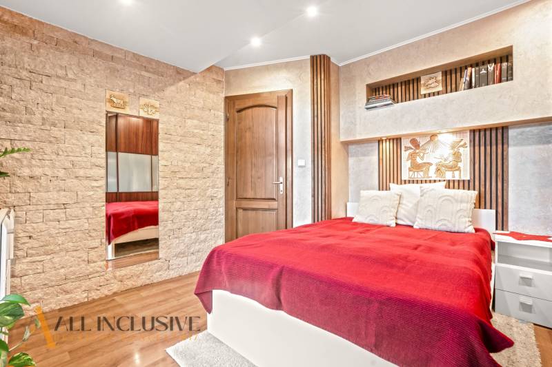 Bedroom in a family house with a bed, stone details, and a wooden decor floor.