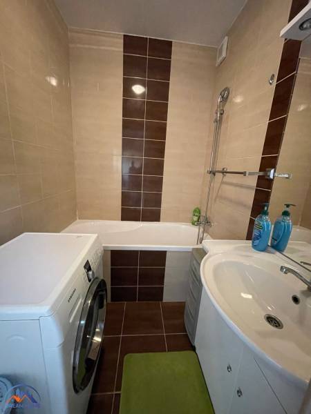 Bathroom in a studio apartment with a bathtub, washing machine, and sink, brown tiles.