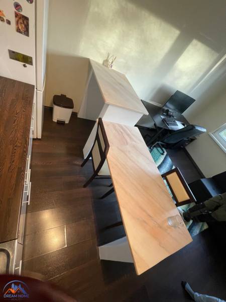 A kitchen in a studio apartment with a wooden floor decor, a bar counter, and a work desk.