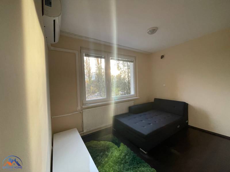 A simple room with a bed, carpet, and window in a studio apartment.