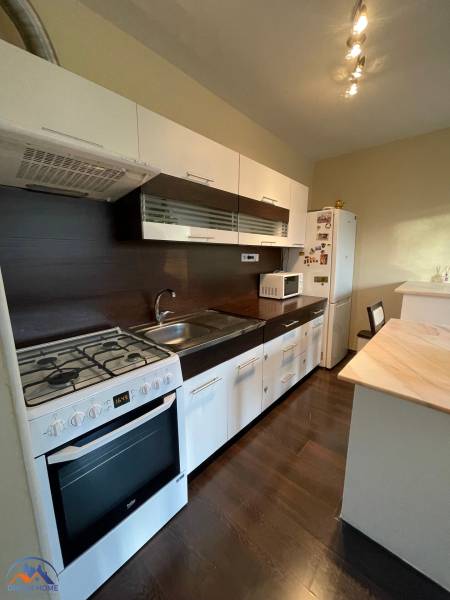 A kitchen in a one-room apartment with a wooden decor floor, a kitchen unit, and a gas stove.
