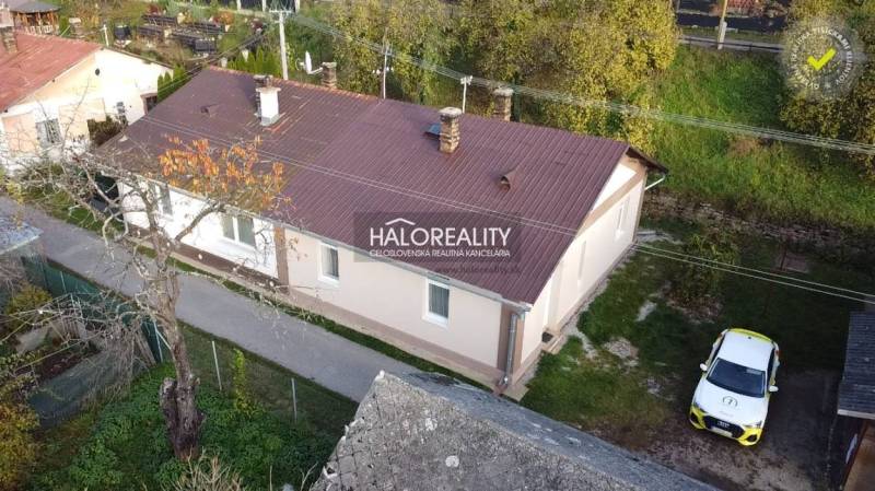 A family house in Sirk with a metal roof, surrounded by a green garden and a car in the yard.