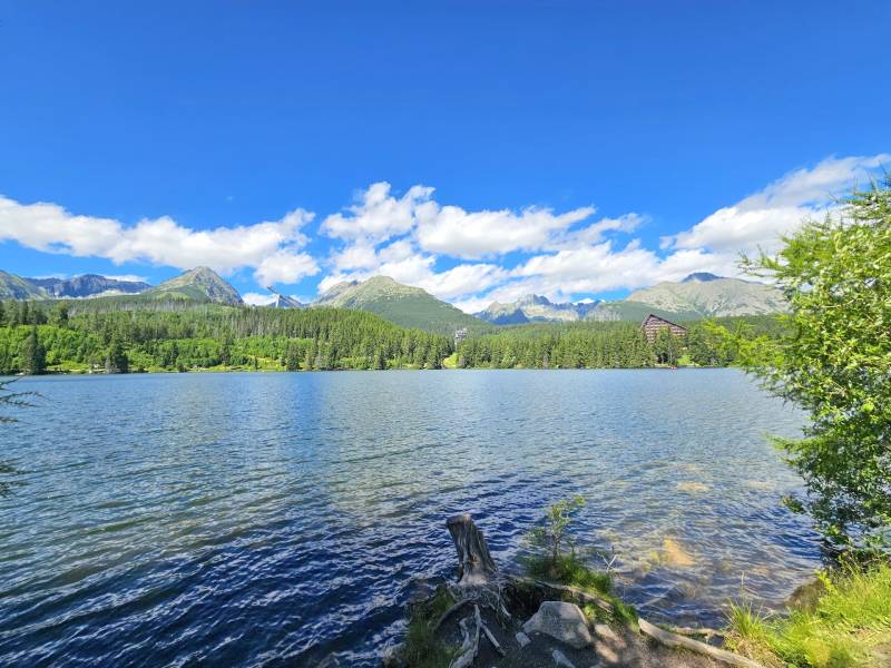 The lake in Štrba surrounded by agricultural and forest lands with mountains and a blue sky.