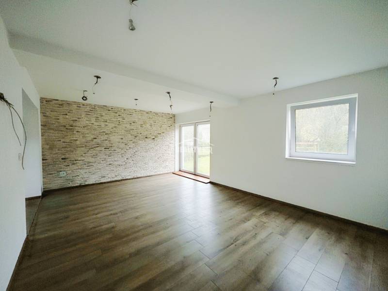 A spacious living room with a stoneware wall and a wooden decor floor in a family house.