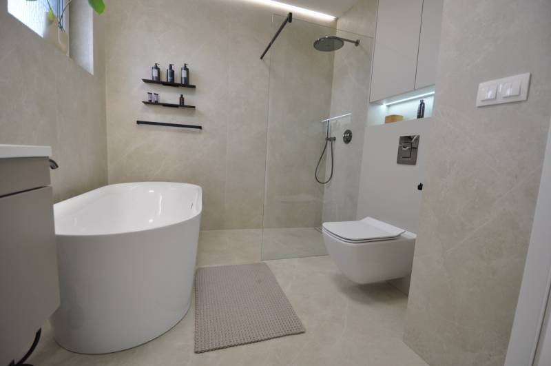 Bathroom in a family house with a bathtub, shower, and toilet, beige tiles.