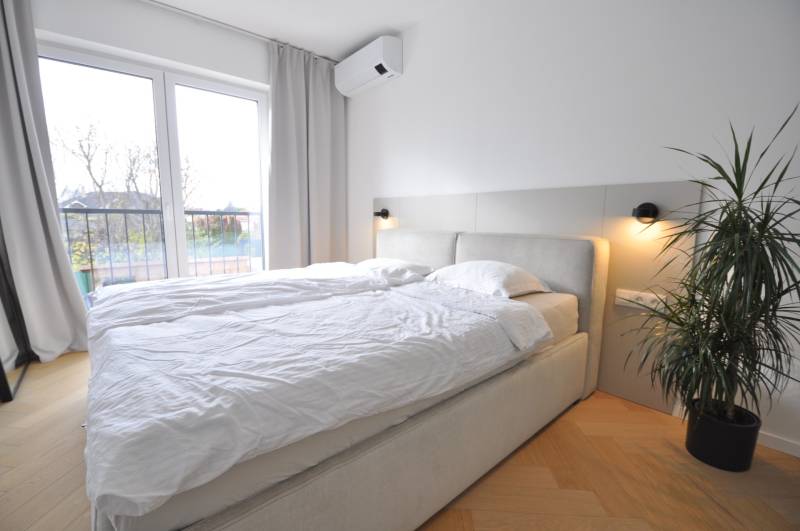 Bedroom in a family house with a bed, plant, and wooden decor flooring.