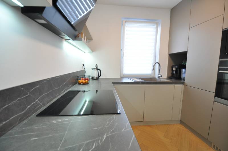 A family house kitchen with a cooktop, sink, and a wooden decor floor.