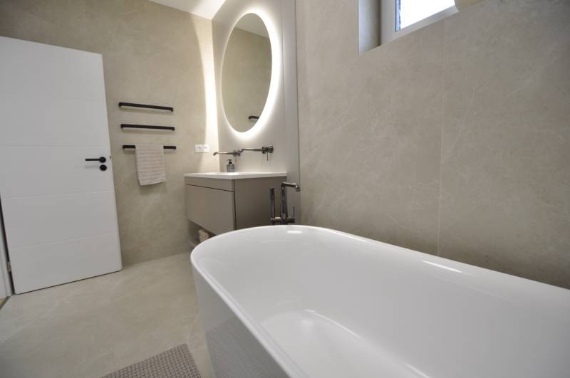 A bathroom in a family house with a freestanding bathtub and an oval mirror.