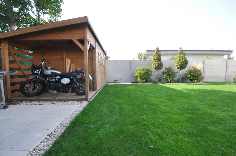 The garden of a family house on Ďuríčkova Street in Miloslavov with a wooden shelter and a motorcycle.