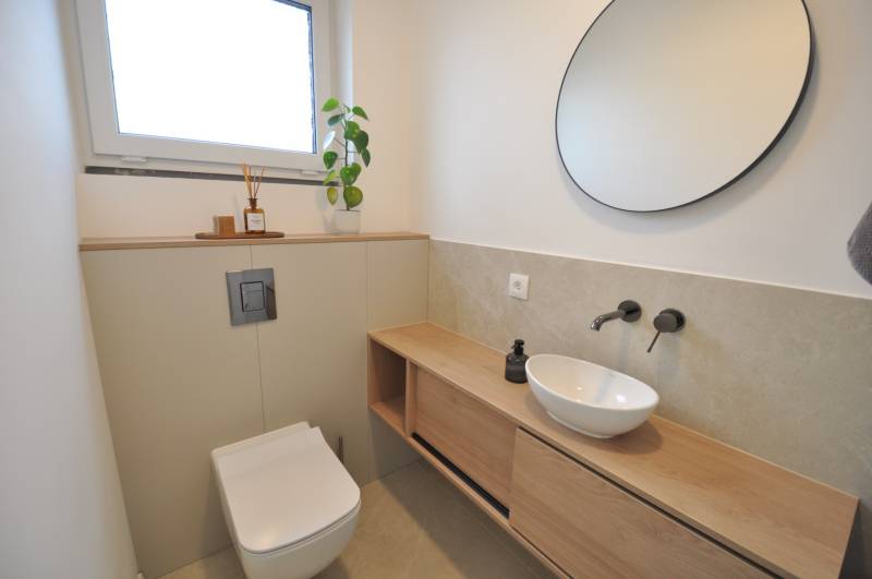 A bathroom in a family house with a round mirror, a sink, and a floor with a wooden decor.