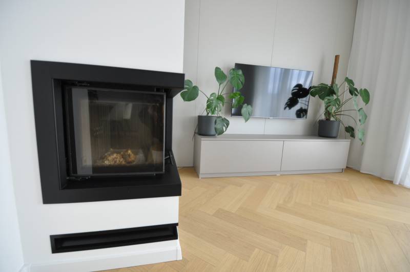 Living room in a family house with a fireplace, television, and wooden decor flooring.