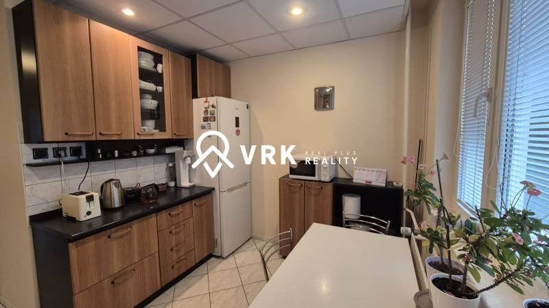 A kitchen in a 3-room apartment with white appliances, a wooden decor floor, and windows with blinds.