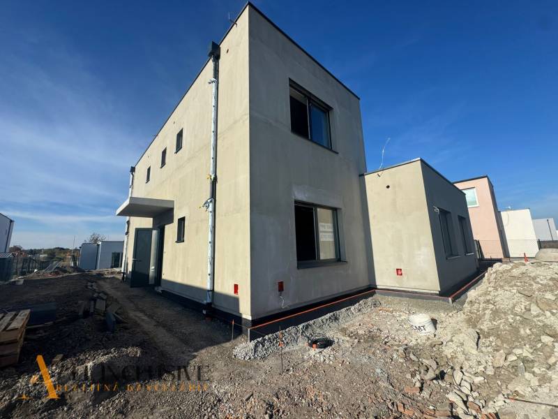 A family house under construction in Hubice, with a minimalist exterior and neighboring buildings.