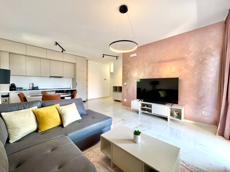 Living room in a studio apartment with a kitchen, gray sofa, television, and dining area.