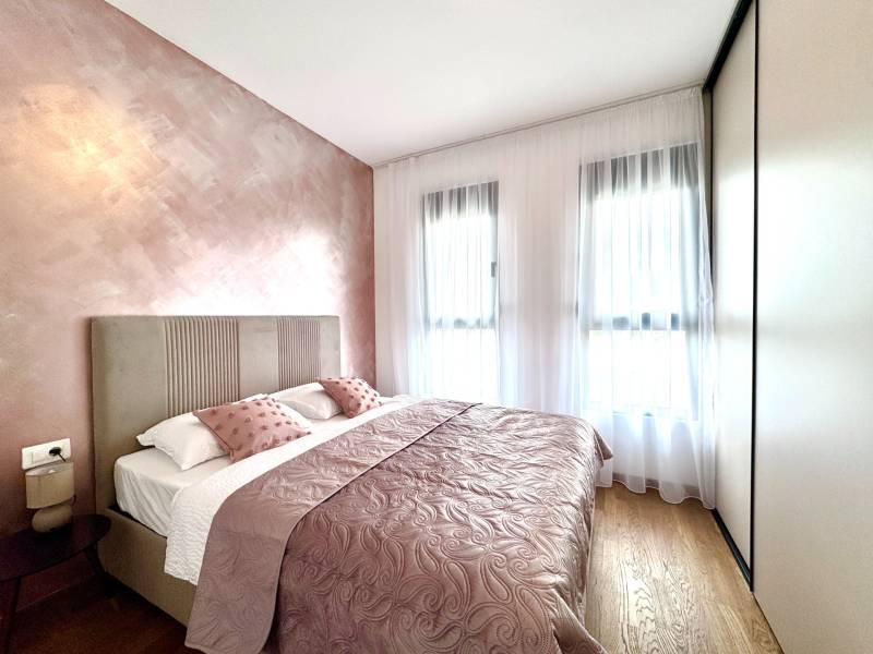 A bedroom in a one-room apartment with pink walls and a wood-patterned floor.