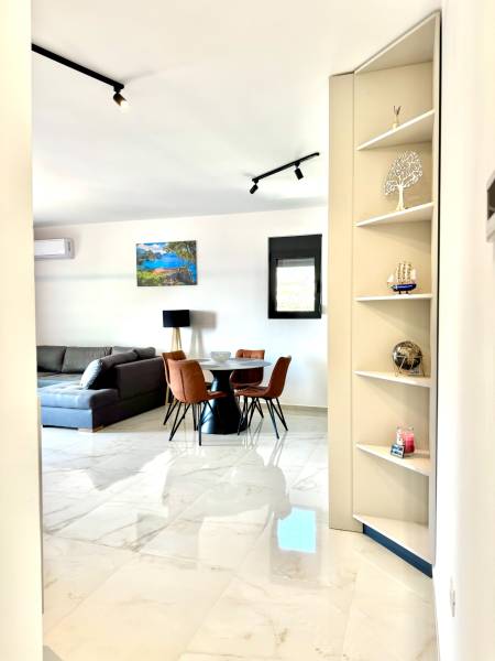 Interior of a 1-room apartment with a white floor, gray sofa, and dining table.