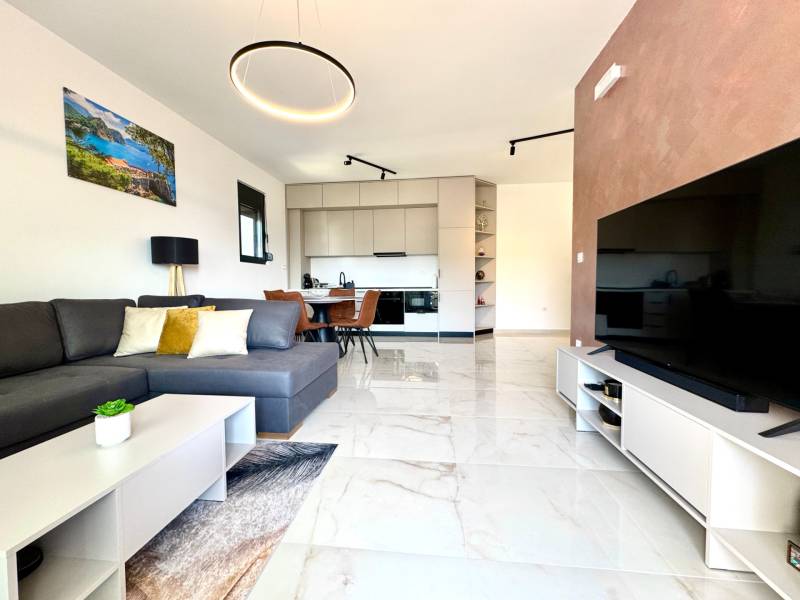 Living room of a one-room apartment with a sofa, TV, and a kitchenette with seating.