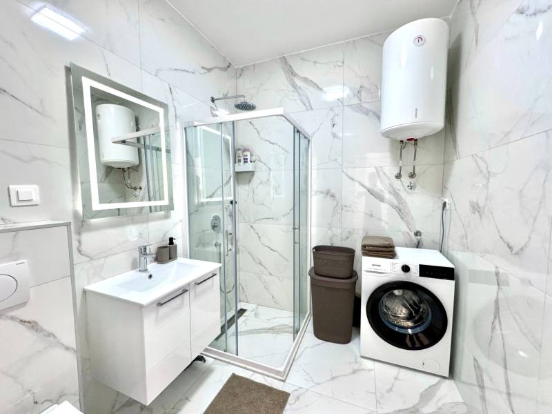 Bathroom in a studio apartment with a shower, washing machine, and elegant marble tiles.