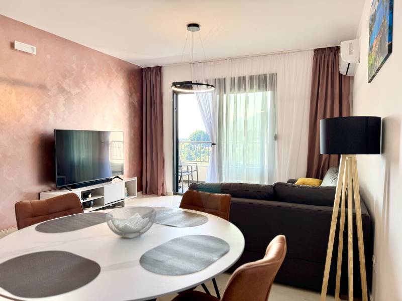 Living room in a one-room apartment with a television, balcony, and an elegant table.
