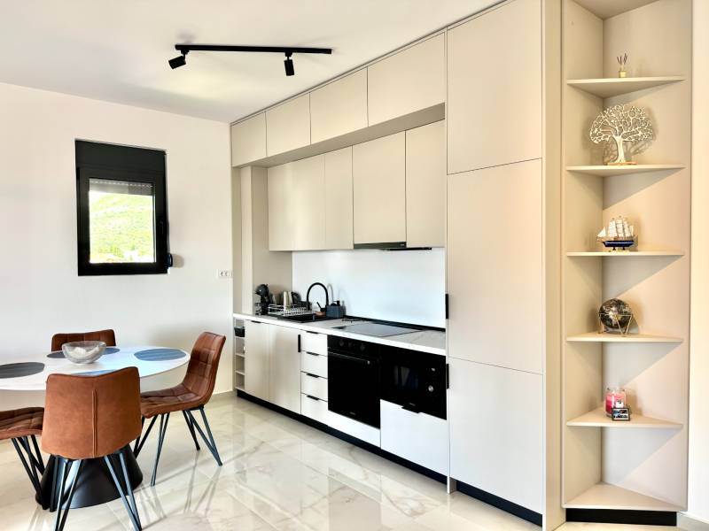A kitchen in a studio apartment with a table, leather chairs, and white cabinets.