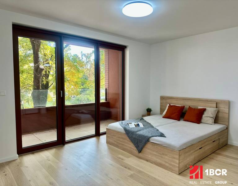 1-bedroom apartment with large windows, wood-patterned flooring, a balcony, and a bed.