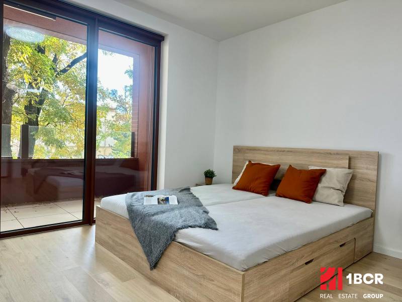 A bedroom with a large window, a bed, and a wooden decor floor in a studio apartment.