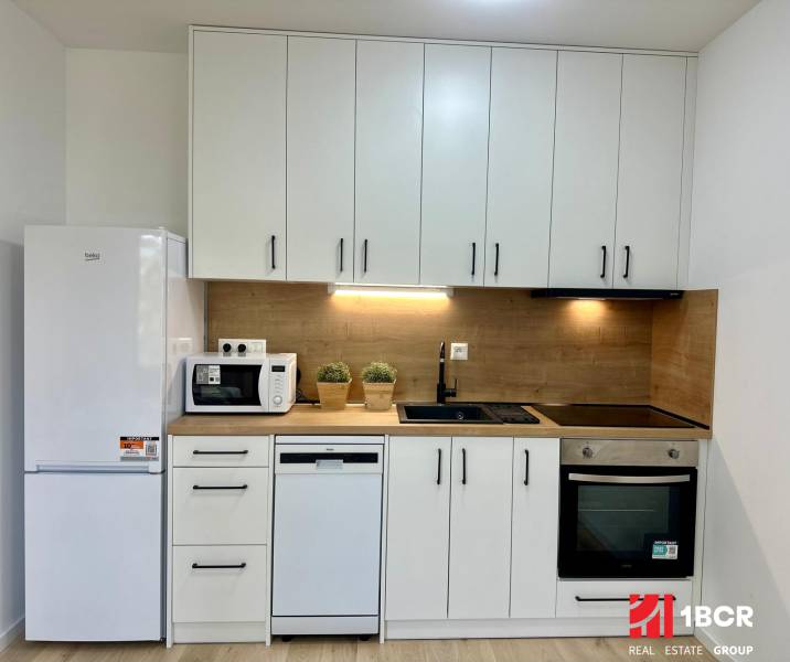 A kitchen with white cabinets, a black sink, and appliances in a studio apartment.
