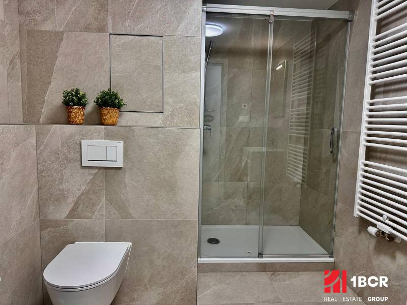 A bathroom in a studio apartment with a toilet, shower, and live plants in baskets.