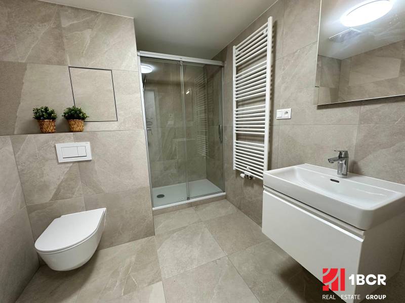 A bathroom in a studio apartment with a toilet, shower, and modern sink.