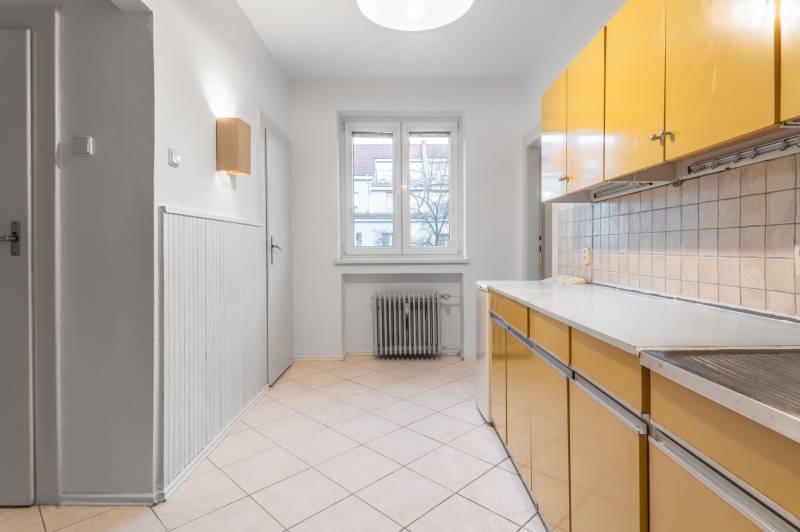 A kitchen in a 3-room apartment with a colorful kitchen unit, a radiator, and tiled flooring.