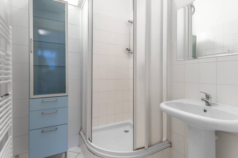 A bathroom with a shower, a sink, and a blue cabinet in a 3-room apartment.