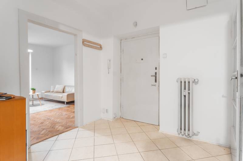A hallway in a 3-room apartment with an entrance door, a radiator, and a view of the living room.