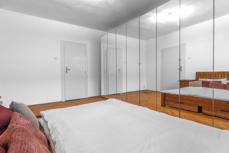 Bedroom in a 3-room apartment with wood-patterned flooring, mirrored wardrobes, and a bed.