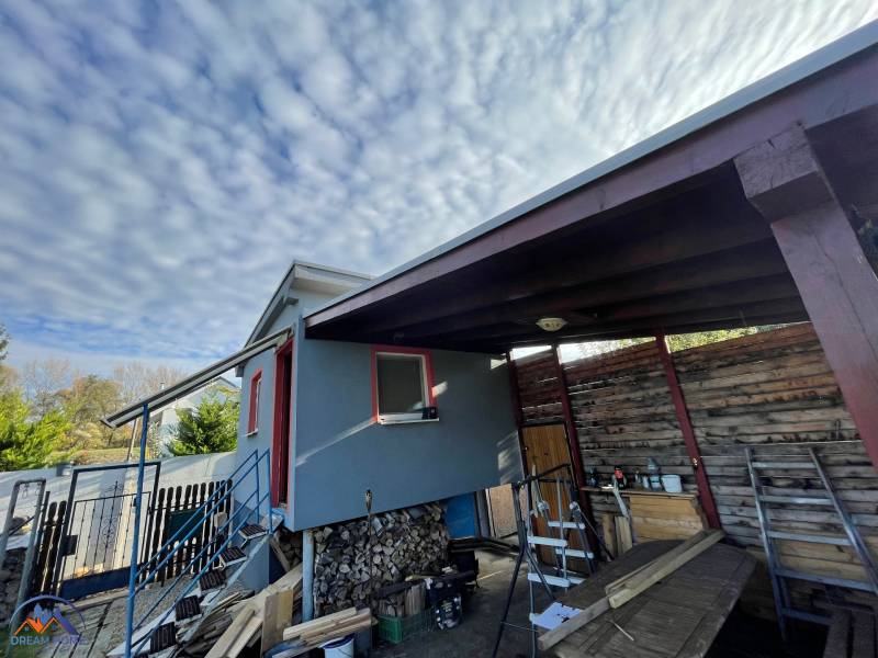 A cottage in Komárno in Nová Osada with a staircase and a wooden shelter under the clouds.