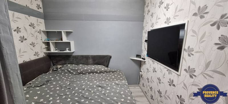 Bedroom in a 3-room apartment with a television, floral wallpaper, and shelves.