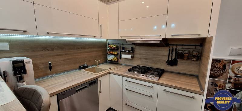 A kitchen in a 3-room apartment with a kitchen unit, extractor hood, appliances, and a floor with a wooden decor.