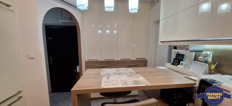 A kitchen in a 3-room apartment with white cabinets and a wooden table, flooring with a wooden decor.