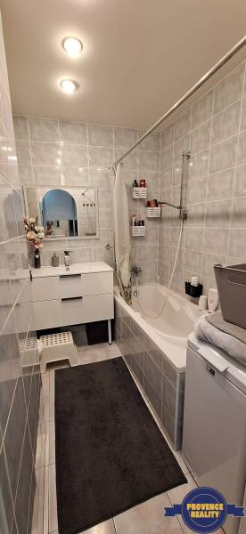A bathroom with light tiles, a bathtub, a sink, and a mirror in a 3-room apartment.