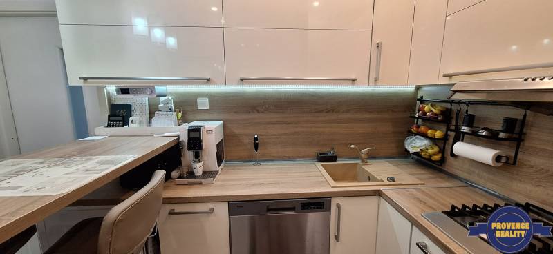 A kitchen in a 3-room apartment with a wooden decor floor, equipped with appliances and a bar counter.