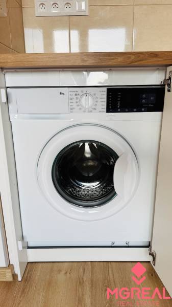 Built-in washing machine in a studio apartment with a wooden decor floor.