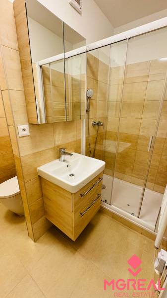 Bathroom with a sink, shower, and tiles in a studio apartment.
