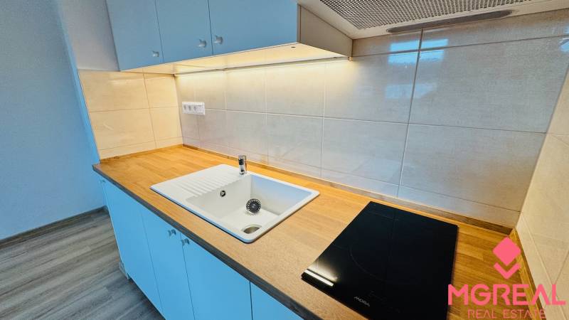 A kitchen unit in a studio apartment with a ceramic sink and a cooktop.