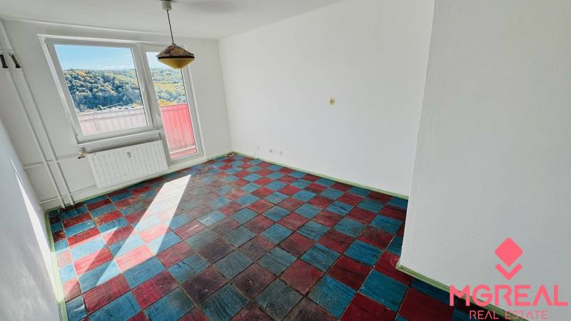 A room in a one-bedroom apartment with a colorful floor and large windows, overlooking nature.