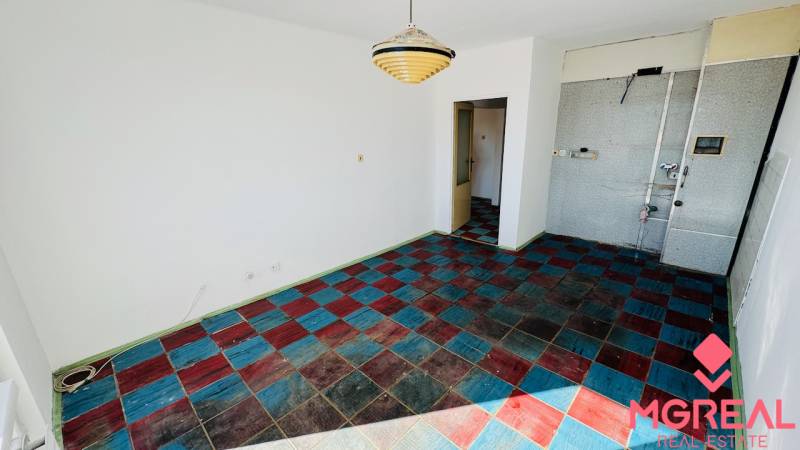 A room in a one-room apartment with a colorful tiled floor and a pendant light.