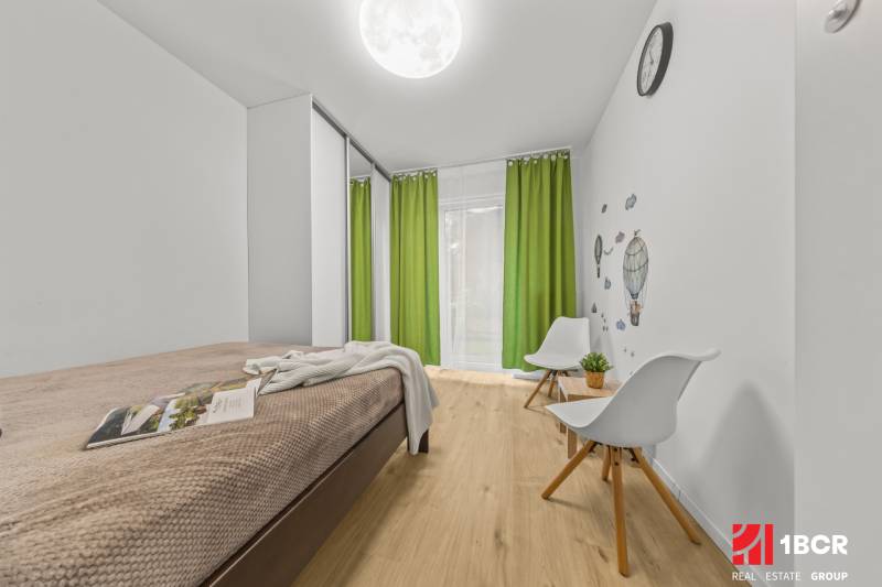A bright room in a 2-room apartment with a bed, green curtains, and a wooden decor floor.