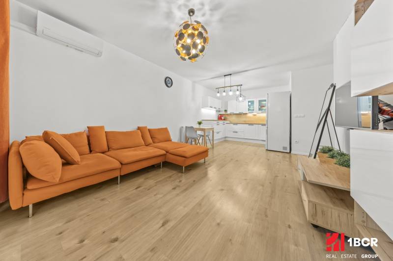 Living room in a two-room apartment with an orange sofa and a wooden decor floor.