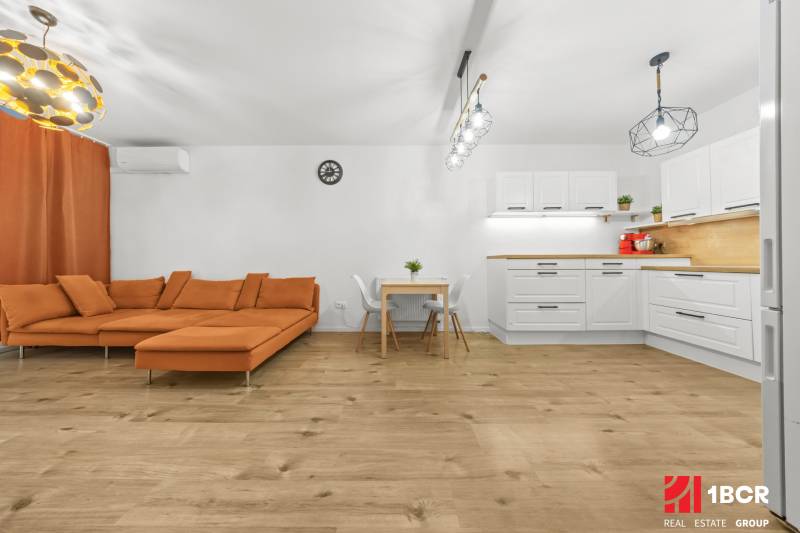 Living room in a 2-room apartment with an orange sofa and a wooden-patterned floor.
